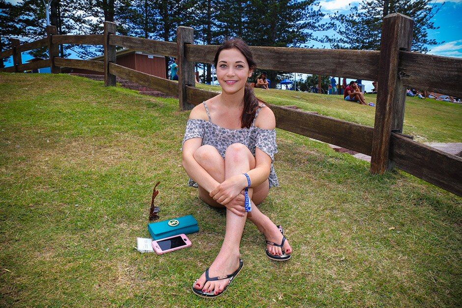 A young woman sitting cross-legged on grass, with a post-and-rail fence behind her.