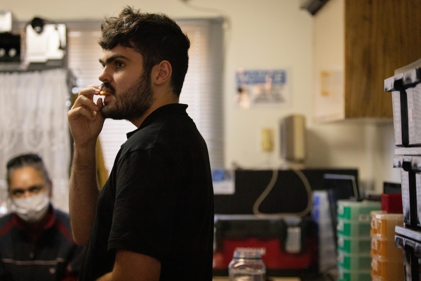 A man sitting on a bench in a workshop eating a snack.