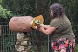 A woman places a bouquet of flowers outside a the entrance to a rural property