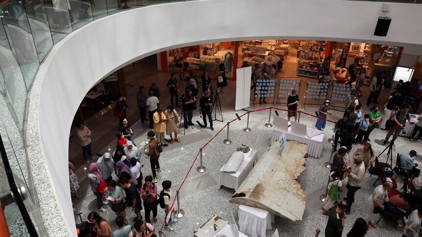 Wreckage that appears to be from an aircraft is displayed in a shopping centre as people stand around. 
