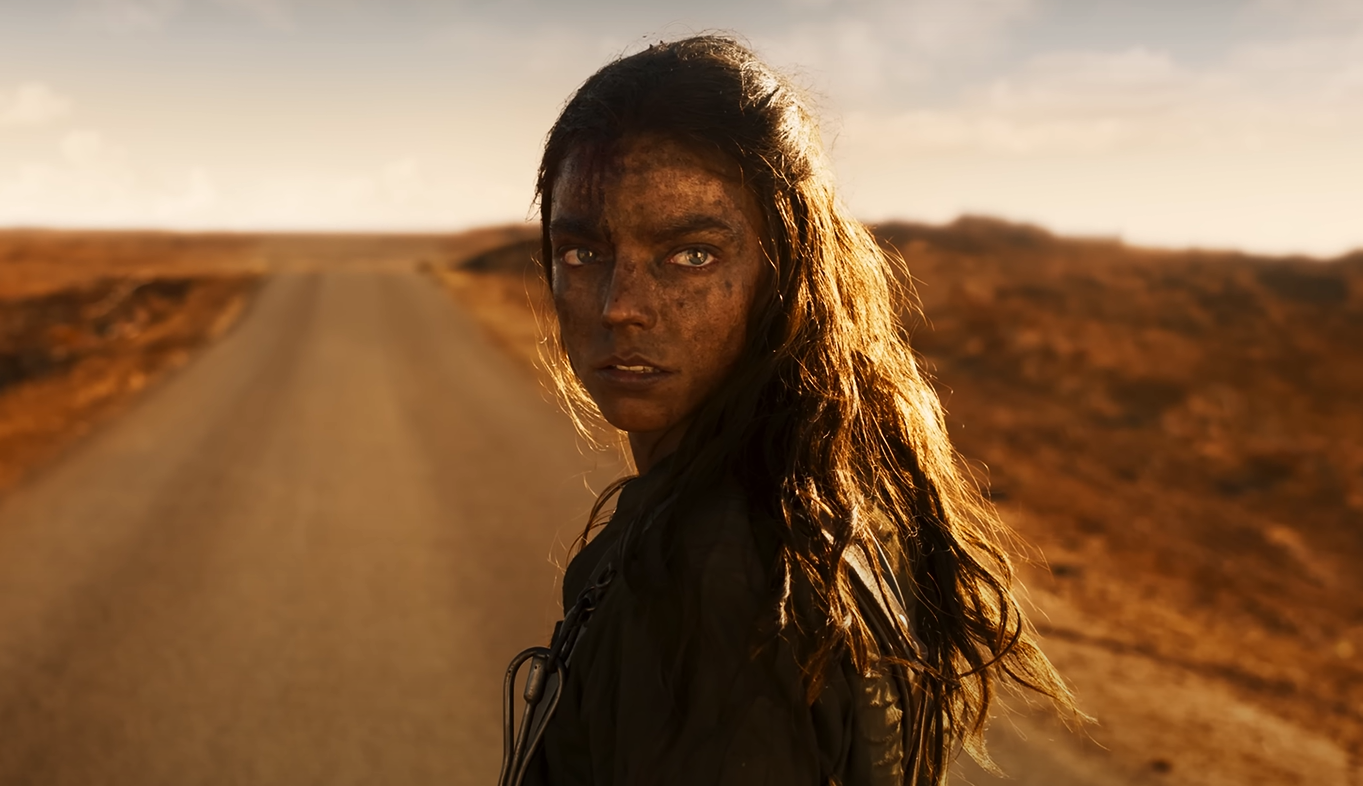 An actress standing in the middle of a dirt road with long hair and a dirty face