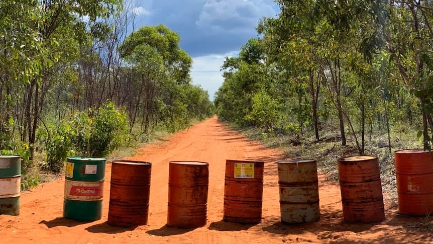 A red road is blocked by fuel drums to prevent entry.