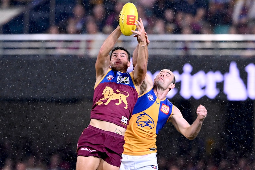 A Brisbane Lons AFL player marks the ball ahead of West Coast Eagles opponent.
