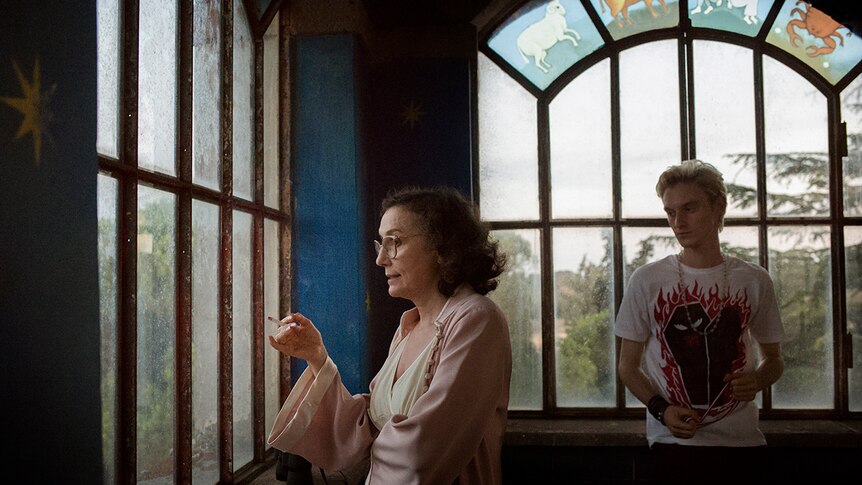 Colour still of Nicoletta Braschi smoking and looking out of a window with Luca Chikovani in 2018 film Happy as Lazzaro.