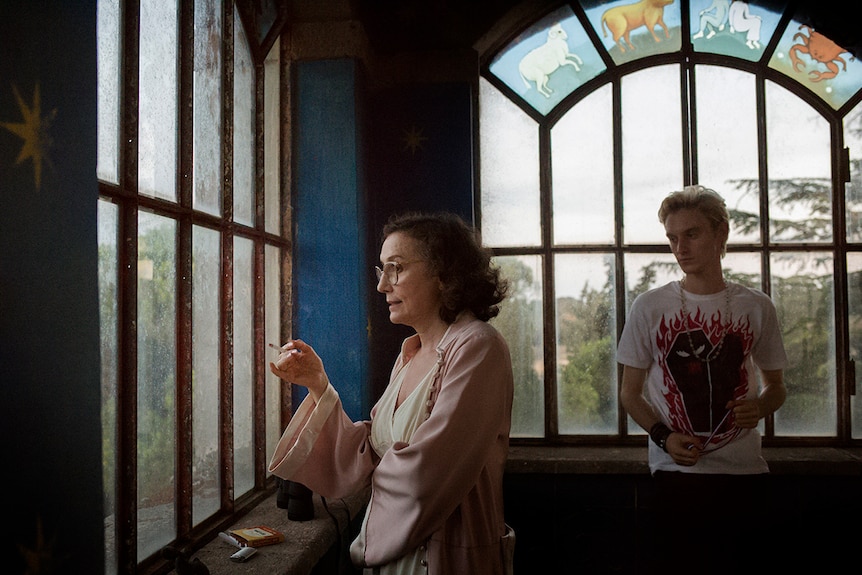 Colour still of Nicoletta Braschi smoking and looking out of a window with Luca Chikovani in 2018 film Happy as Lazzaro.