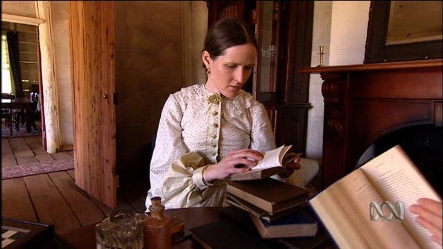 Woman in period costume reads book in house