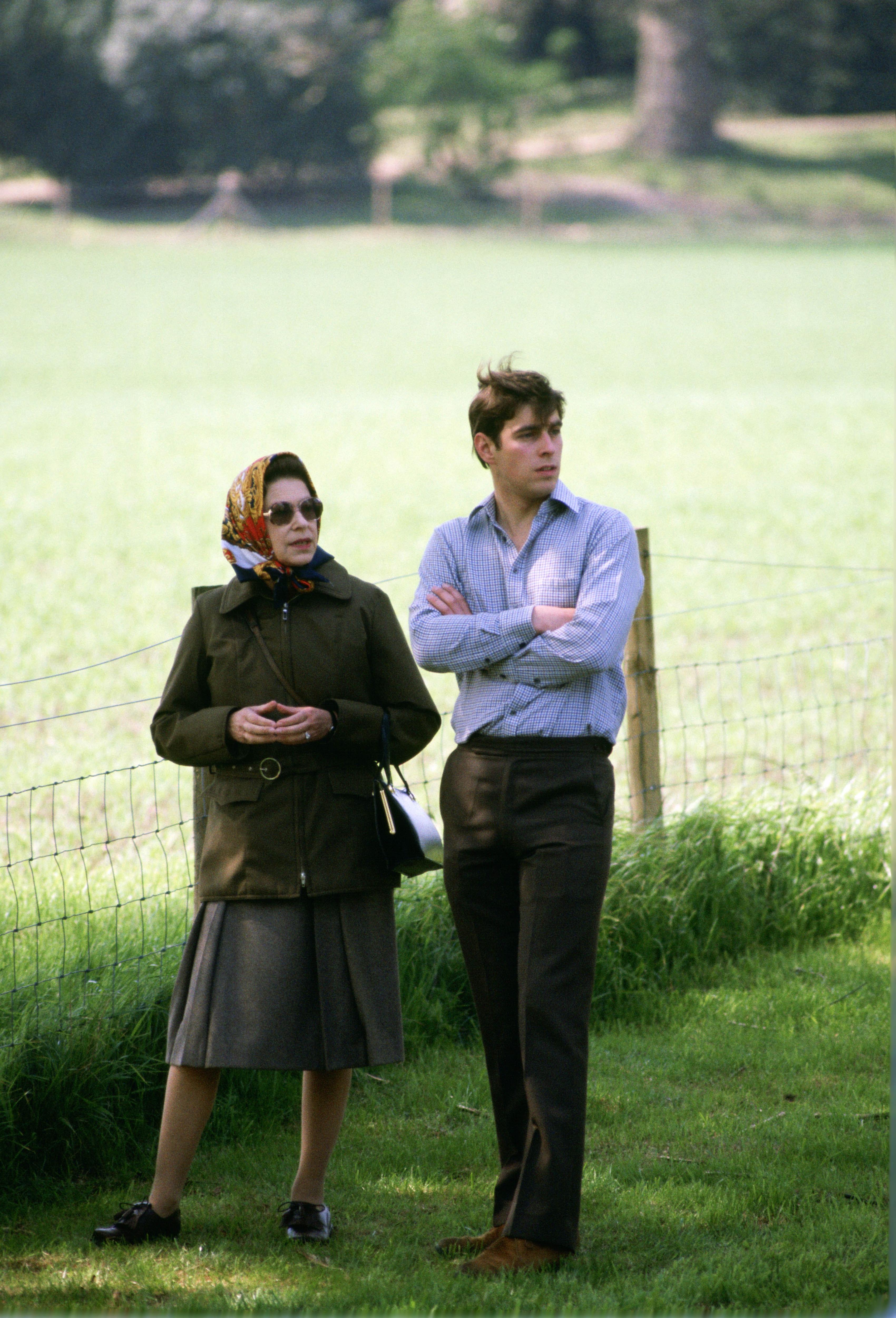 A woman in a headscarf and glasses walks through a grassy field with a young man