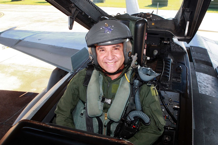 Andrew Nikolic sits in the passenger seat of an F/A-18 Hornet wearing a flying suit and helmet.