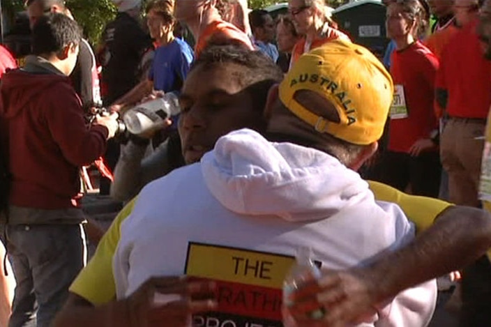 An Indigenous man being hugged, with a group of people in the background.