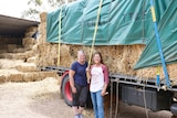 Two women stand in front of a loaded truck filled with hay.