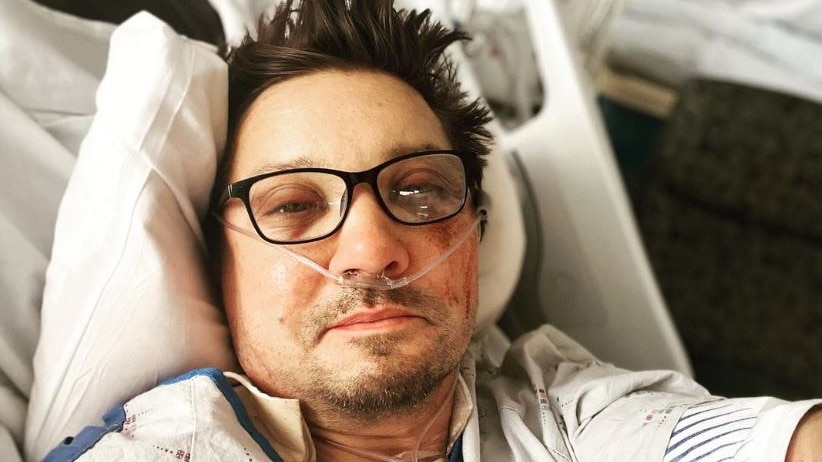Renner poses for a selfie while lying in a hospital bed with a graze on his face and tubes in his nose. 