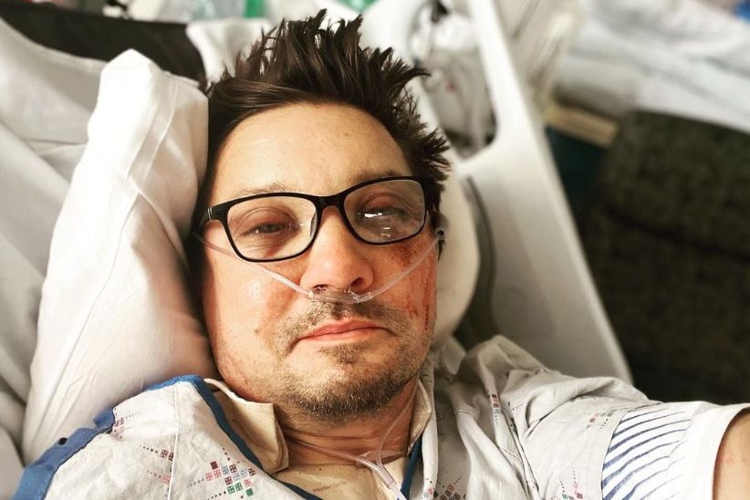 Renner poses for a selfie while lying in a hospital bed with a graze on his face and tubes in his nose. 