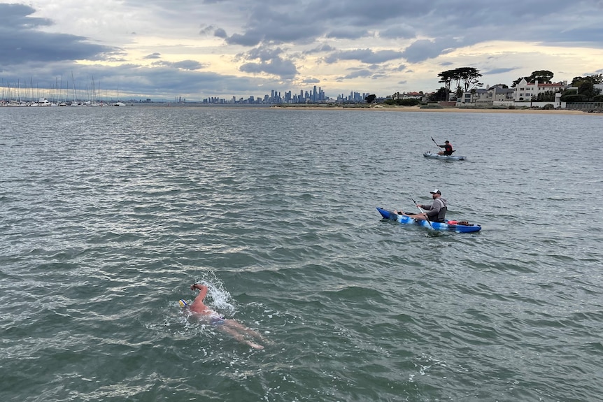 A man swimming in ocean water with a kayak.