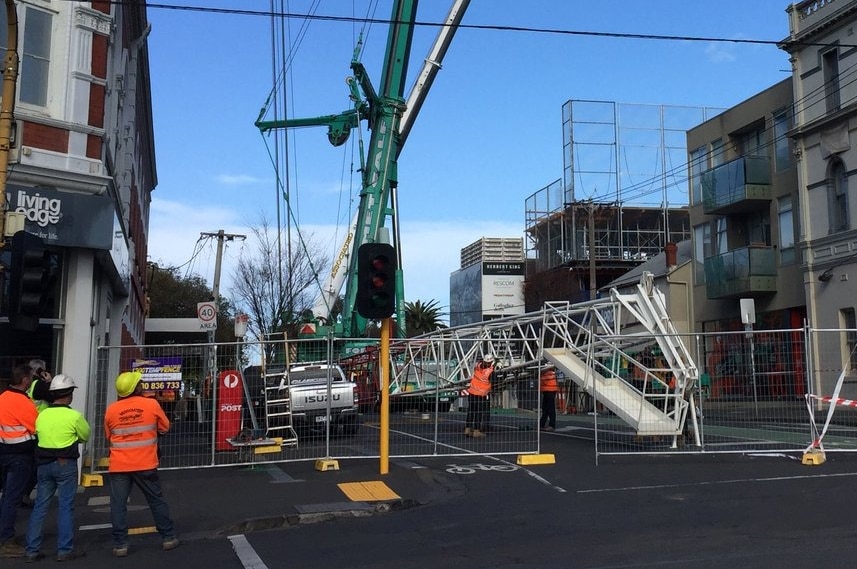 The boom from a damaged crane is lowered to the ground by workers using  as second crane.