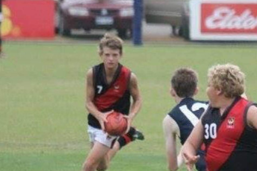 Old image of three boys playing football in red and black tops.