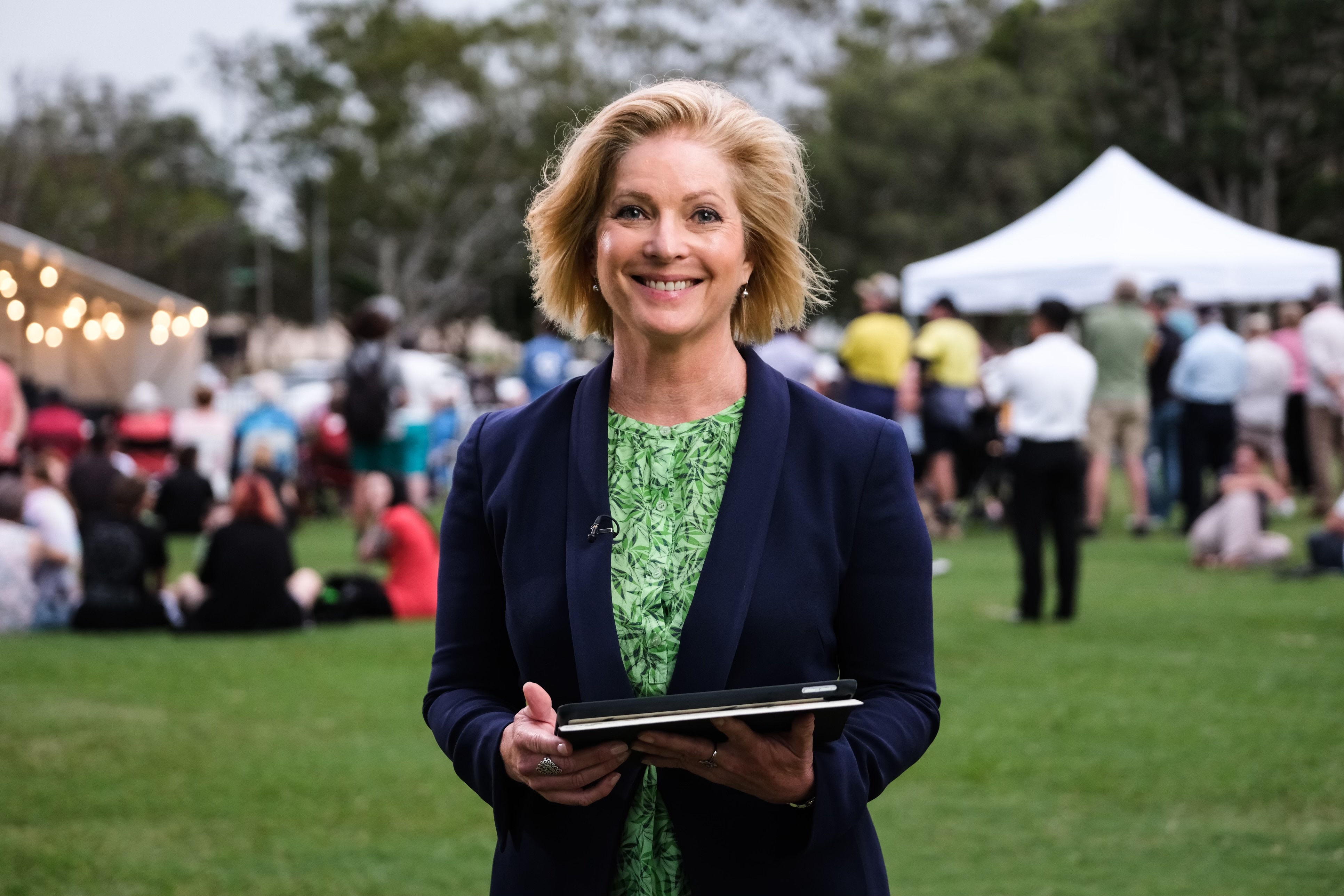 A woman wearing professional clothes smiles in a park filled with people