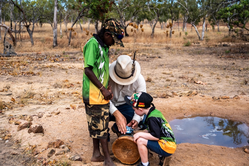 A teacher and two students look over a spy camera set up near a watering hole