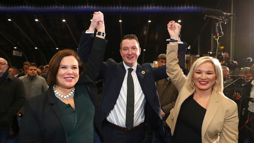 In a busy conference hall, three politicians raise their hands up in victor as they pose for the cameras.