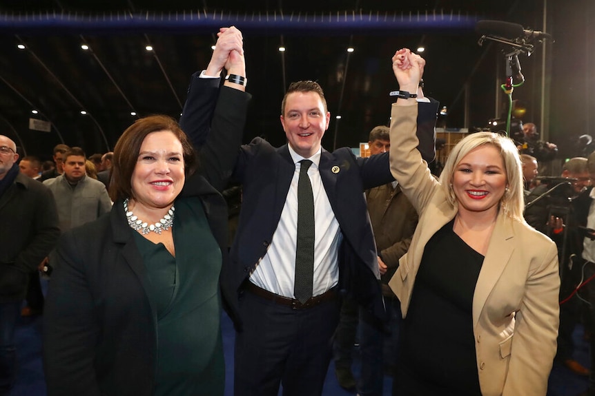 In a busy conference hall, three politicians raise their hands up in victor as they pose for the cameras.