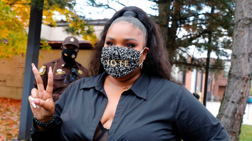 Rapper Lizzo makes the peace sign while wearing a black and white mask saying 'vote'