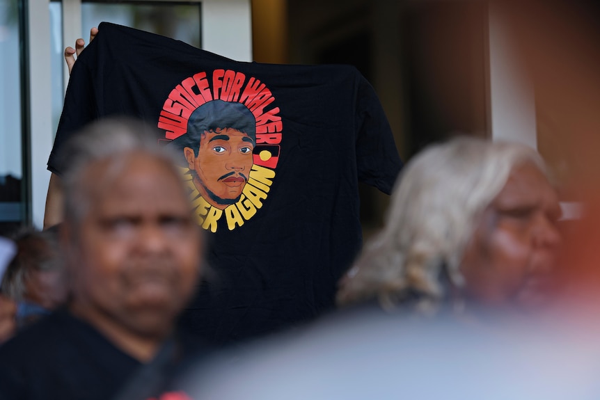 A person holds a t-shirt with the words 'justice for walker, never again' above their head. 