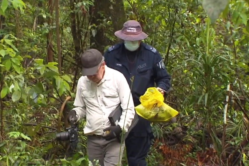 two men walking in the dense bush, one with a yellow bag