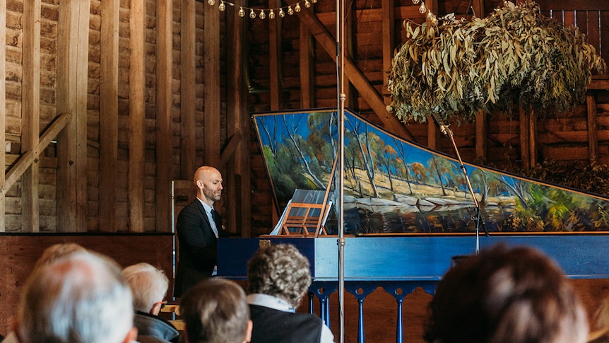 Erin Helyard performs on a blue harpsichord in a wooden barn.