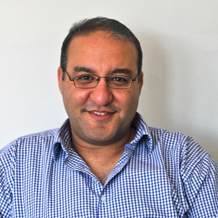 A man wearing glasses and a blue checked shirt smiling.