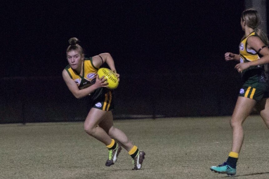 Marissa Williamson-Pohlman playing Australian rules football during a night match, with a teammate near them