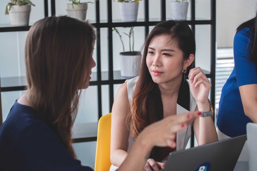 Two women speaking and gesturing in front of a laptop.