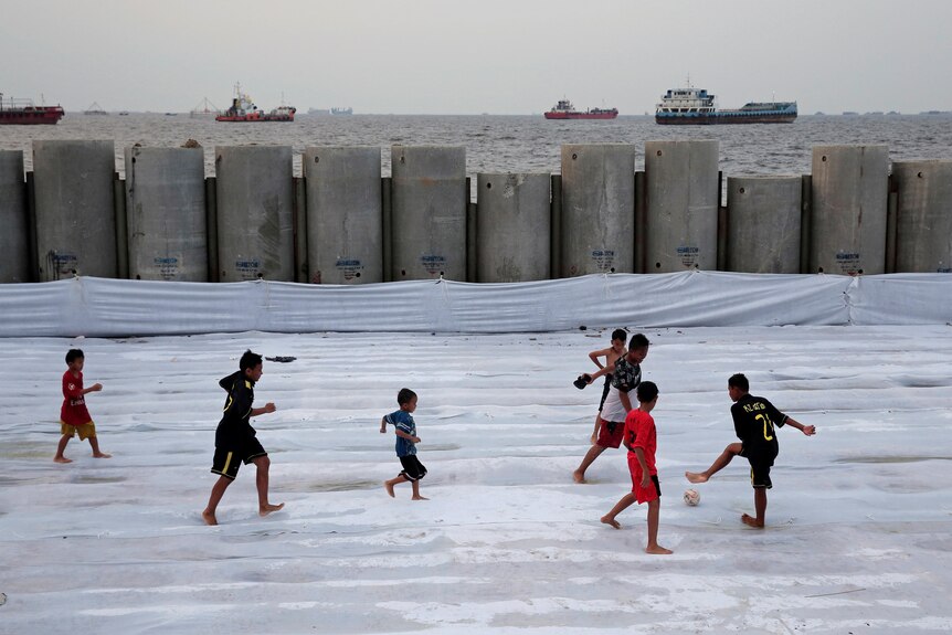 Children play soccer near a new construction of a concrete sea wall.