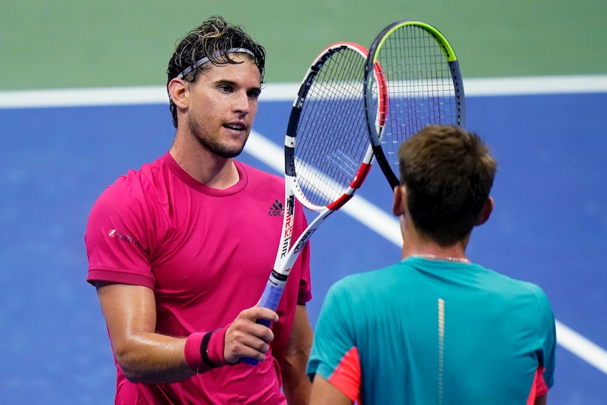 Two tennis players stand raising their racquets to each other at the end of a match.