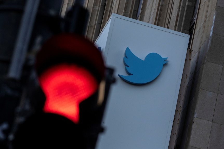 The Twitter logo on a building photographed behind a red traffic light. 