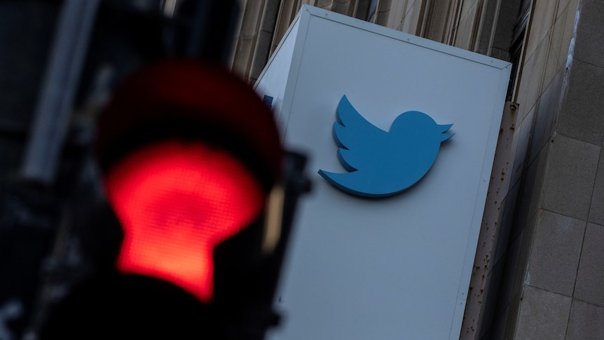 The Twitter logo on a building photographed behind a red traffic light. 
