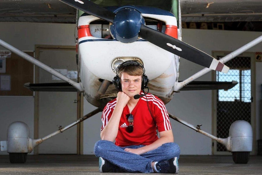 A young man sits in front of a plane.