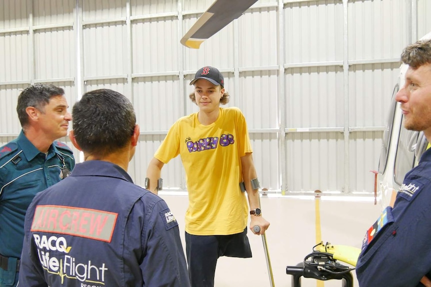 Ned Desbrow stands with crutches while talking to paramedics who helped save his life.