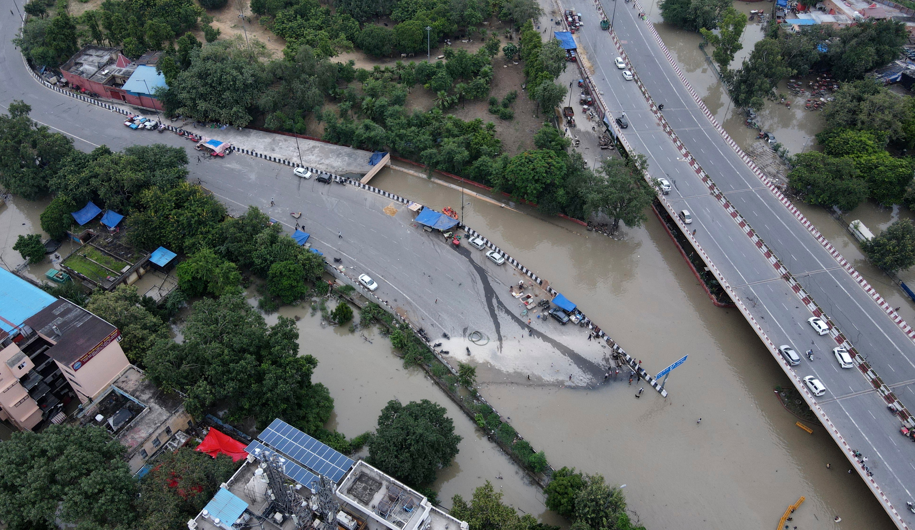 An aerial view of a highway over another major road shows the lower road completely cut off by brown floodwaters