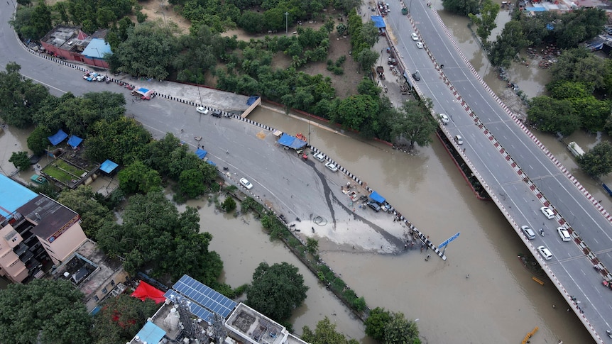 An aerial view of a highway over another major road shows the lower road completely cut off by brown floodwaters