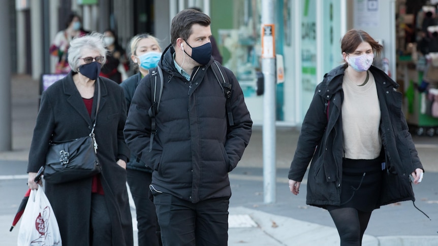 Various people walk through Canberra wearing facemasks 