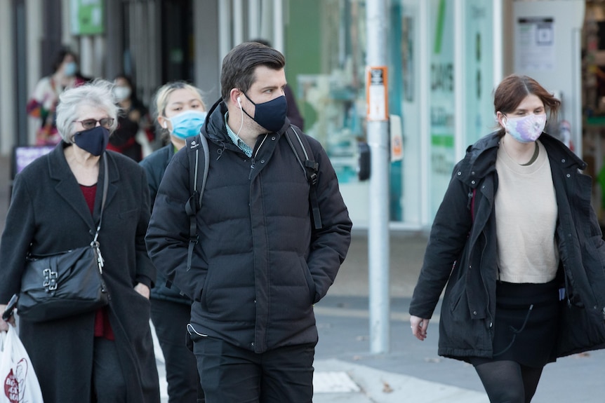 Various people walk through Canberra wearing facemasks 