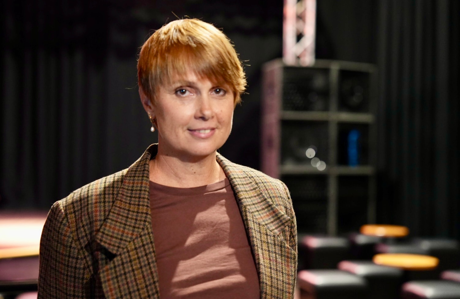 Adele tiene el pelo corto y claro y viste una chaqueta a cuadros mientras sonríe para una foto en un teatro musical.