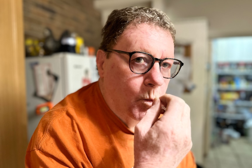 A man with greying hair and glasses holds a syringe in his mouth.