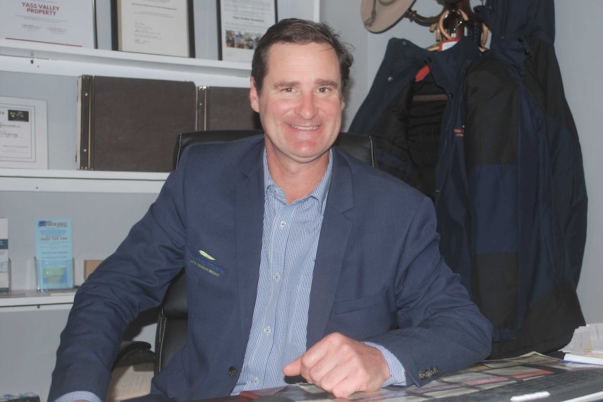 Real estate businessman sits at office desk in country town practice.