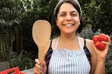 Jaclyn Crupi stands while holding a wooden spoon and tomatoes.