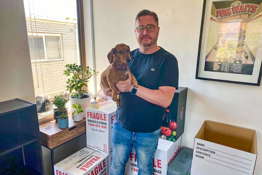 Paul Menz holding his small dachshund, surrounded by boxes.