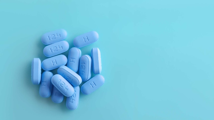 Open bottle of blue prescription PrEP Pills on blue background.