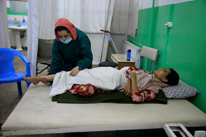 An Afghan girl lies on a bed while receiving medical care from a health worker
