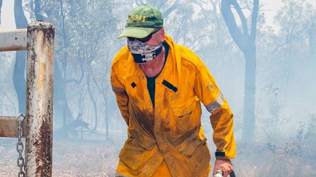 A man in a bight yellow shirt and pants runs with a firefighting hose in hand. His nose and mouth are covered by a mask.