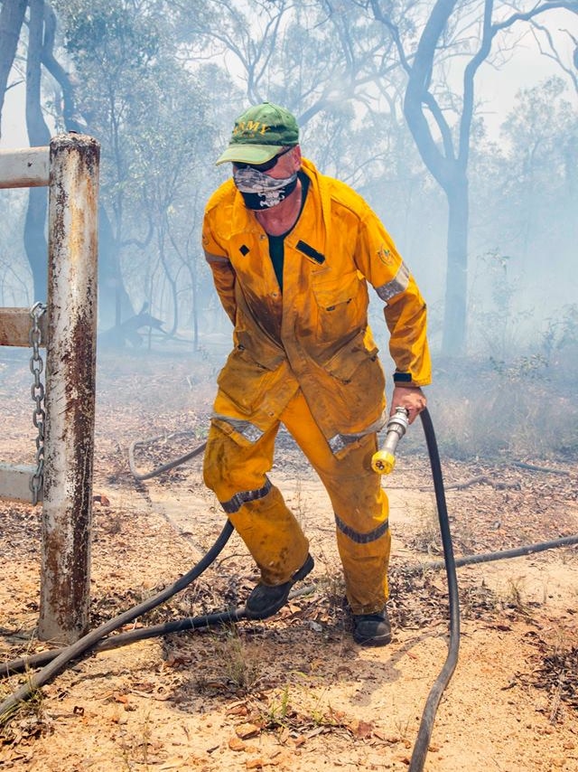 A man in a bight yellow shirt and pants runs with a firefighting hose in hand. His nose and mouth are covered by a mask.