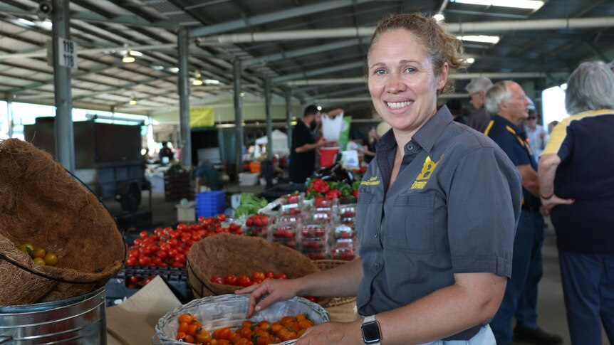 A woman smiles in a large shed in front of a basket of tomatoes.